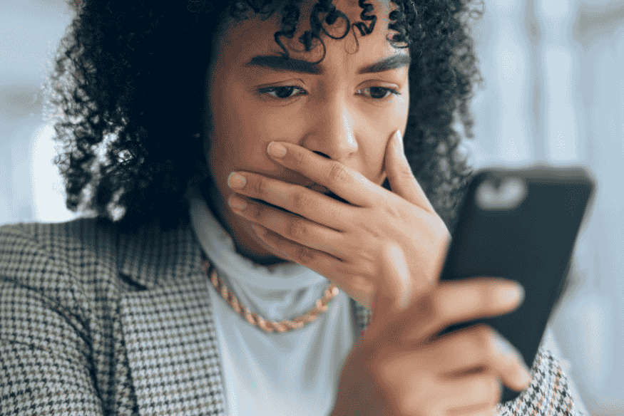 Mulher assustada olhando para o celular, representando preocupação ao identificar possíveis golpes em negociações de dívidas.
