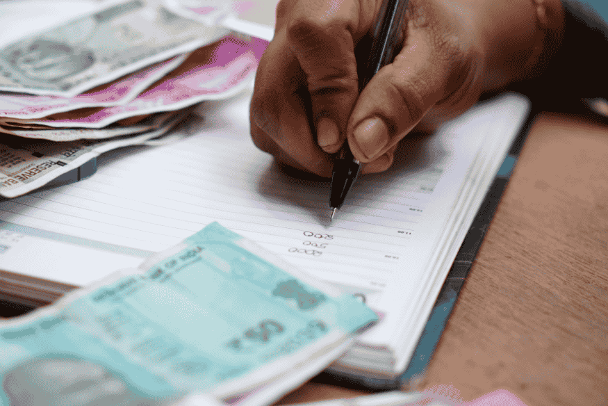 Pessoa fazendo anotações financeiras em caderno, ao lado de cédulas de dinheiro, representando o planejamento do uso do 13º salário e renda extra para pagar dívidas.
